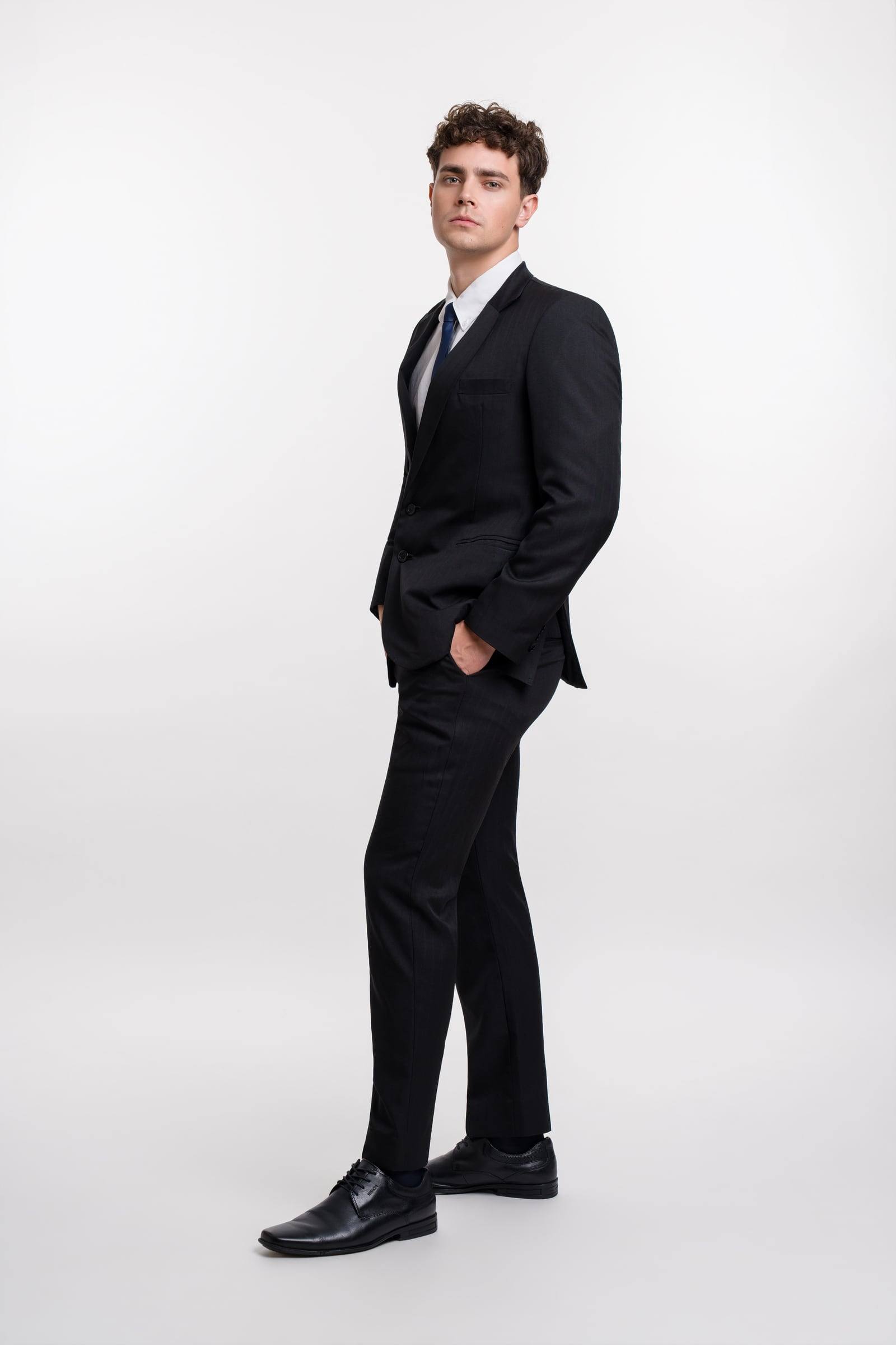 Jorge Tyrakowski in a black suit, white shirt and navy tie, full length, hand in pocket