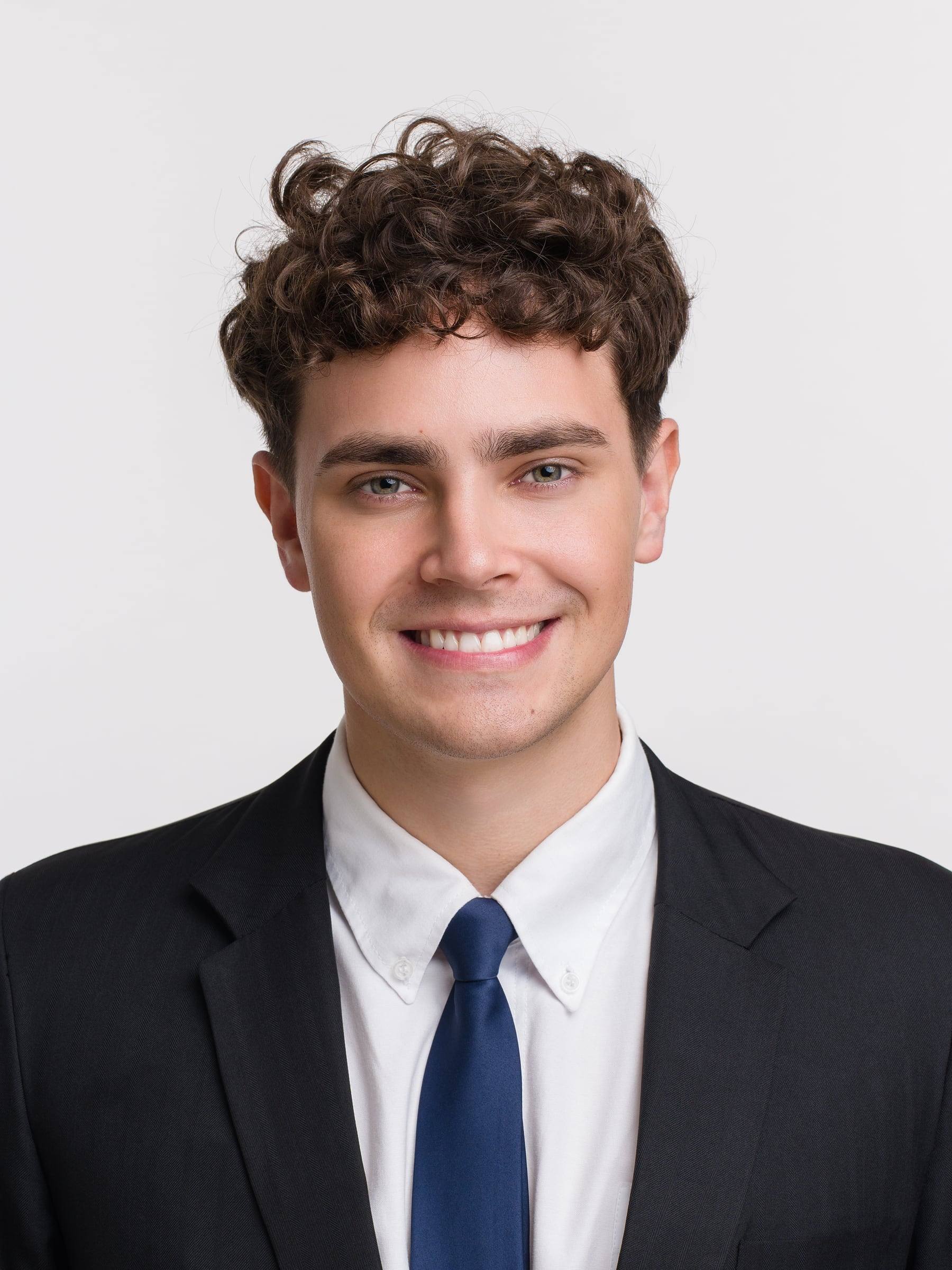 Jorge Tyrakowski in a black suit, white shirt and navy tie, smiling headshot
