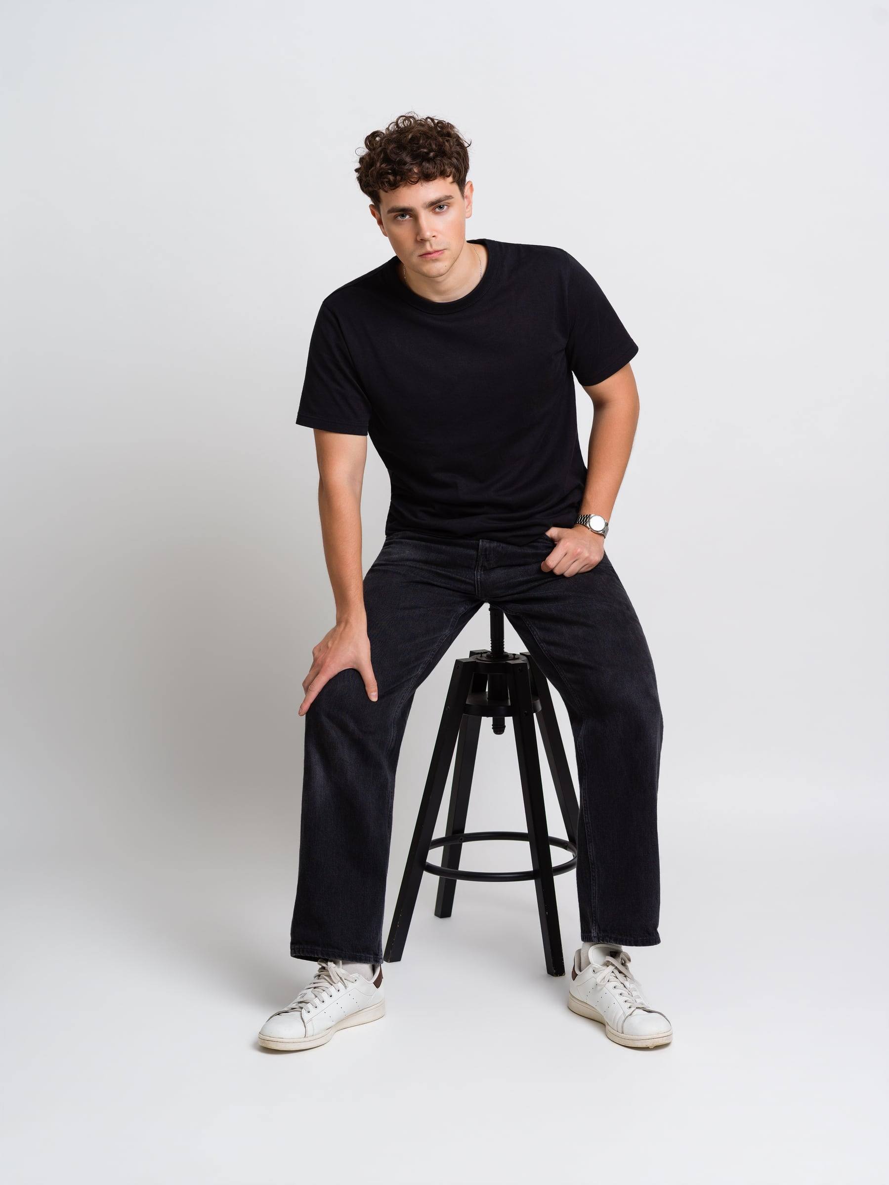Jorge Tyrakowski in a black T-shirt and black jeans, seated on a stool