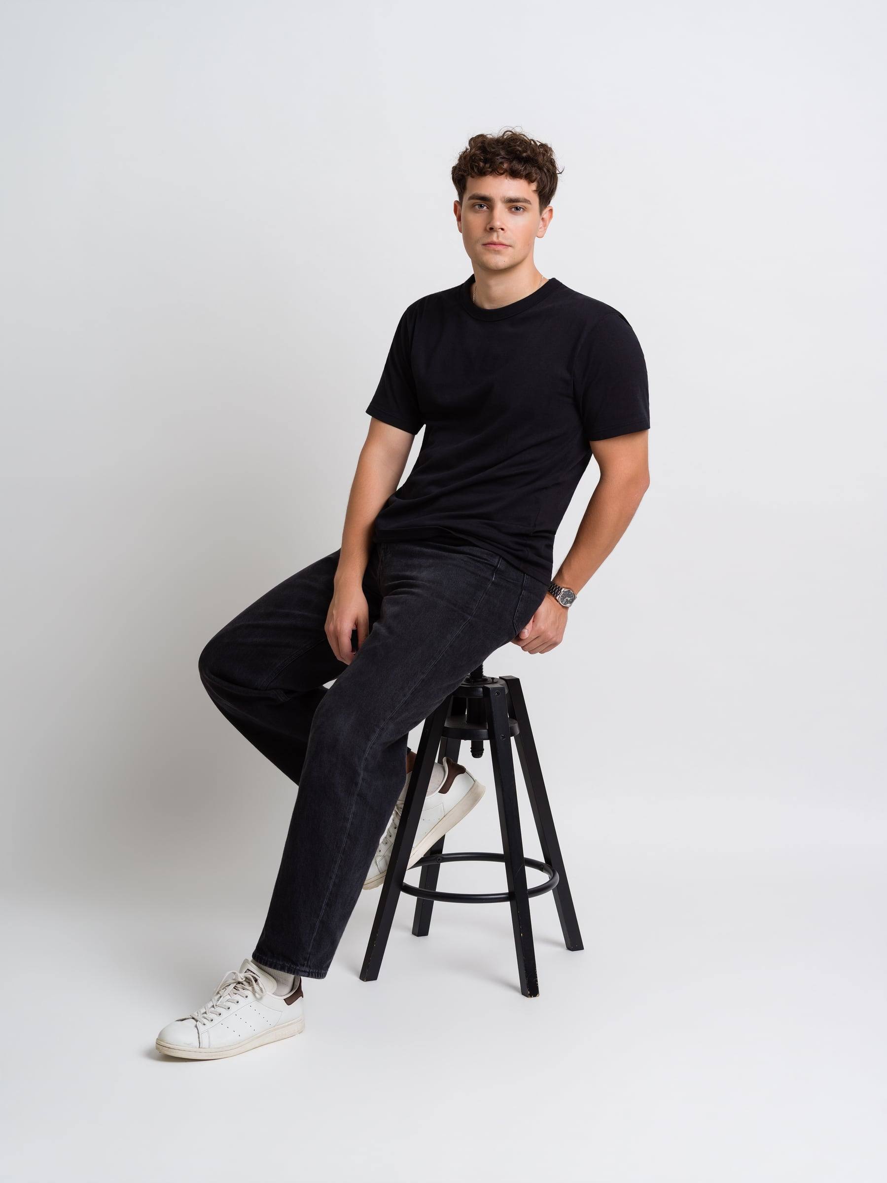 Jorge Tyrakowski in a black T-shirt and black jeans, seated, looking away
