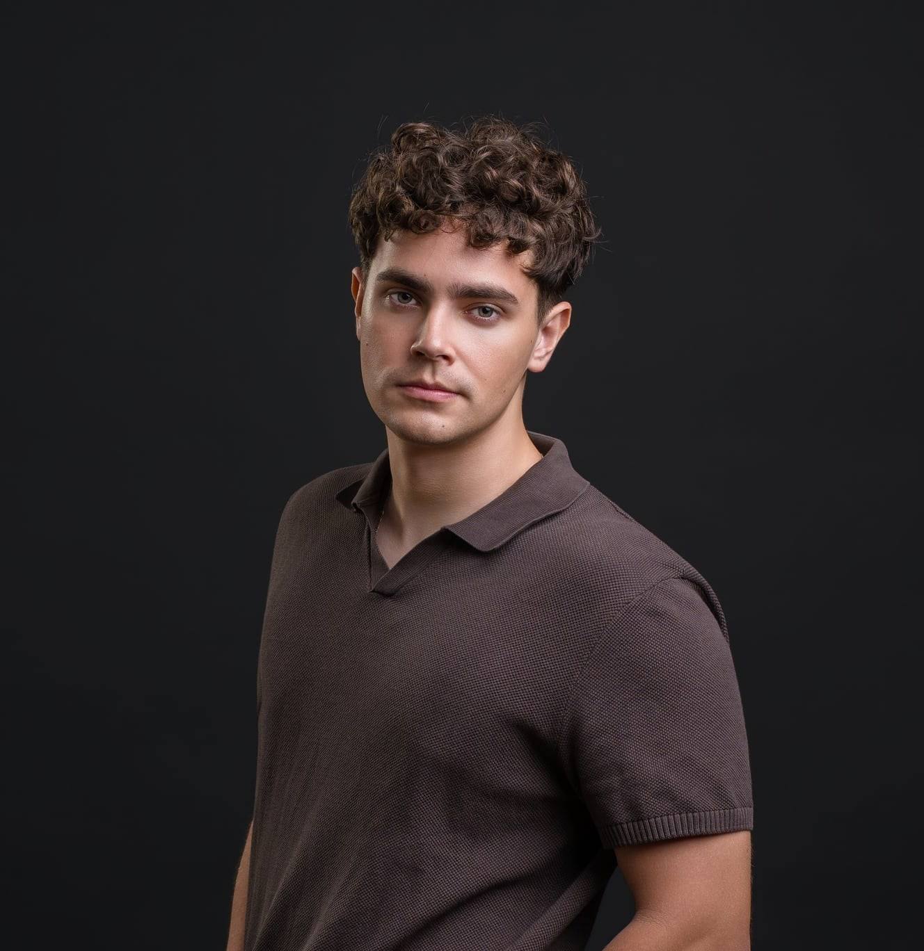 Jorge Tyrakowski, half-length portrait in a brown knit polo against a black studio backdrop